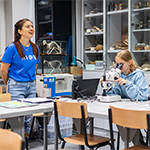 trwają warsztaty w laboratorium, na pierwszym planie prowadząca i dwie nastolatki przy mikroskopach